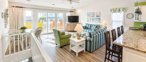A spacious living area with a sofa set, a television, and a dining area with chairs.