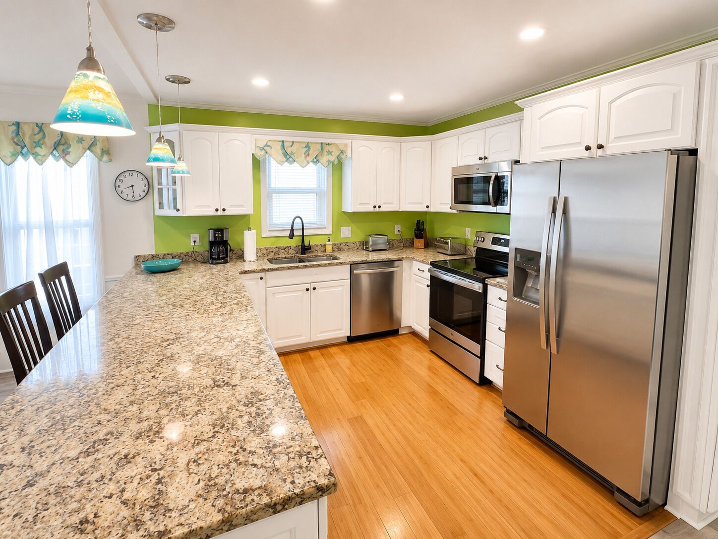 A kitchen with white cabinets, stainless steel appliances, a granite countertop, and a clock on the wall.