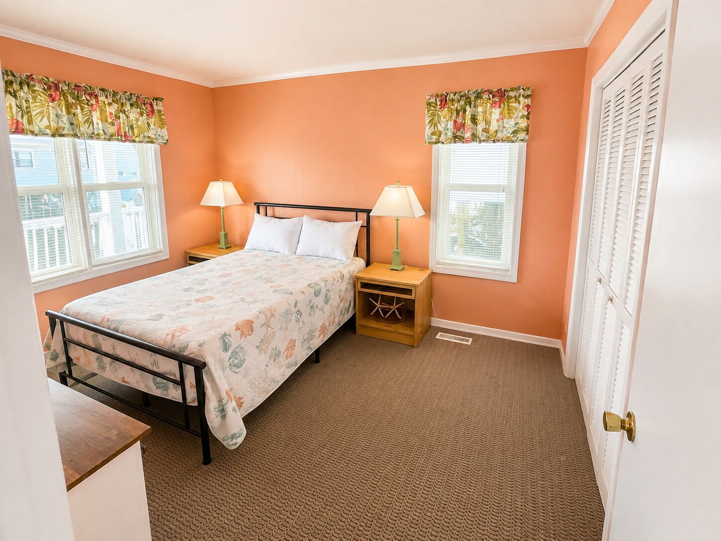 A bedroom with a bed, two nightstands, two lamps, a window with blinds, and a door.