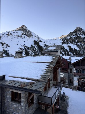 Un refugi de muntanya d'arquitectura de pedra, amb un balcó de fusta i vistes a vessants cobertes de neu.