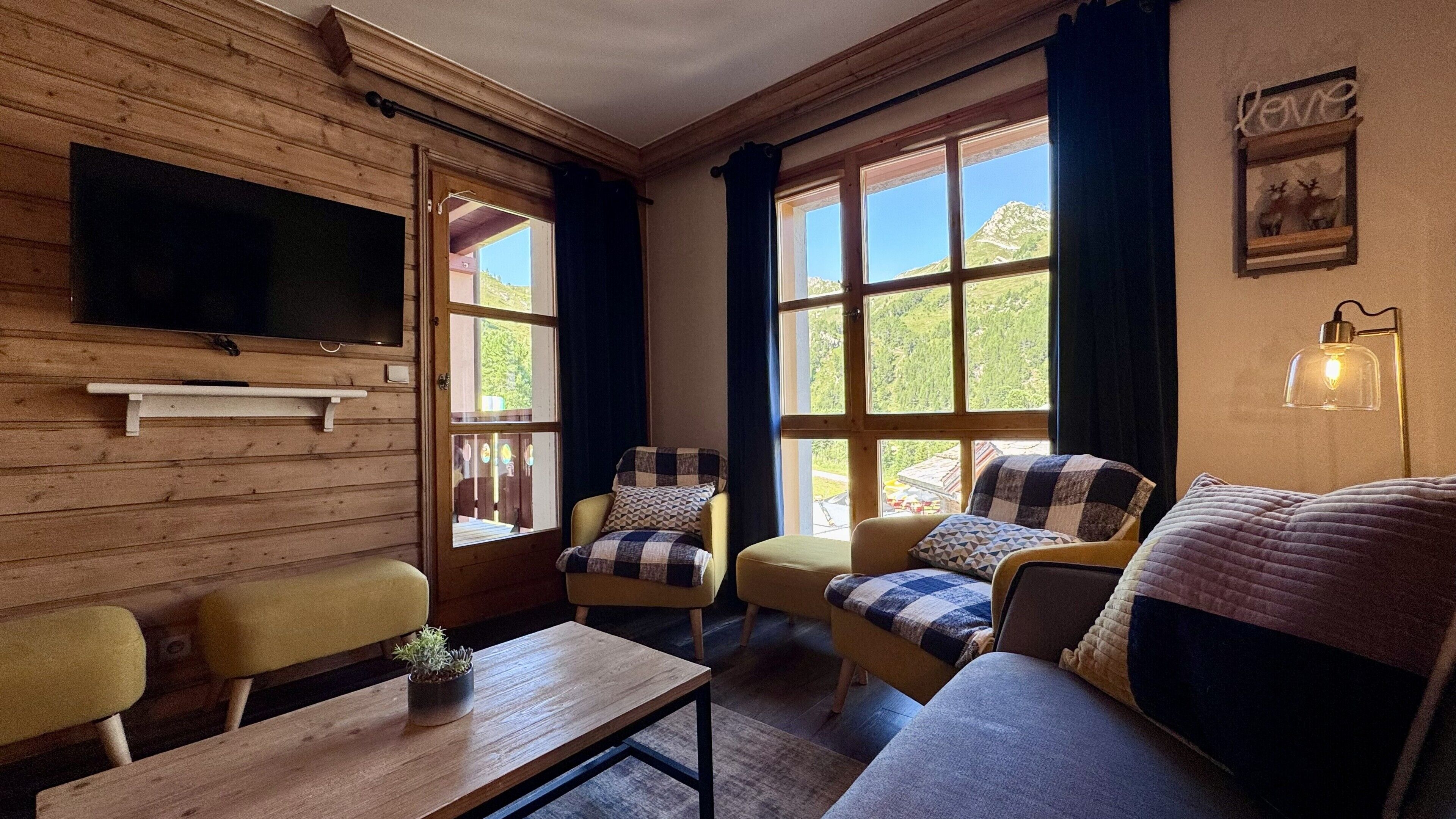 A cozy room with wooden walls, a flat-screen TV, and a large window offering a mountain view.