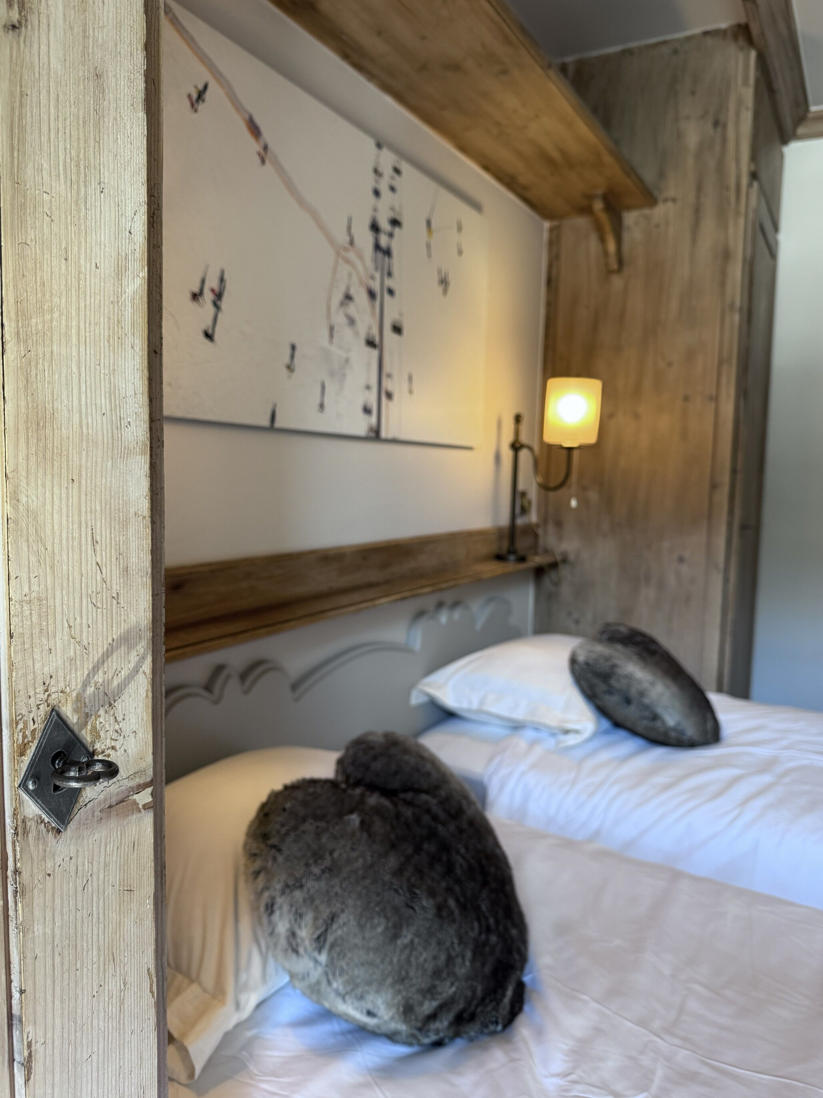 A bedroom with two beds, a wooden headboard, a wall-mounted artwork, and a bedside lamp.