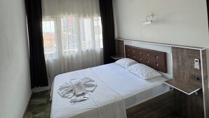 A hotel room with a bed, a bedside table, an air conditioning unit, and a window with curtains. - Öz tralles otel (Aydın)