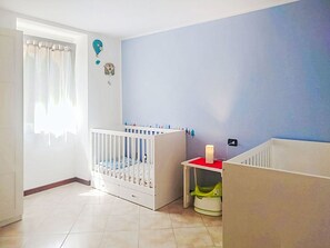 Ein Babyzimmer mit einem Kinderbett, einem Wickeltisch und einem Fenster mit Vorhängen.