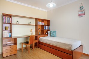 Ein Schlafzimmer mit einem hölzernen Bett, einem Schreibtisch mit Büchern, einem Stuhl und einem kleinen Tisch.