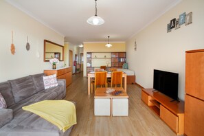 Ein Wohnzimmer mit Sofa, Couchtisch, TV-Schrank und einem Essbereich mit Stühlen und Tisch.