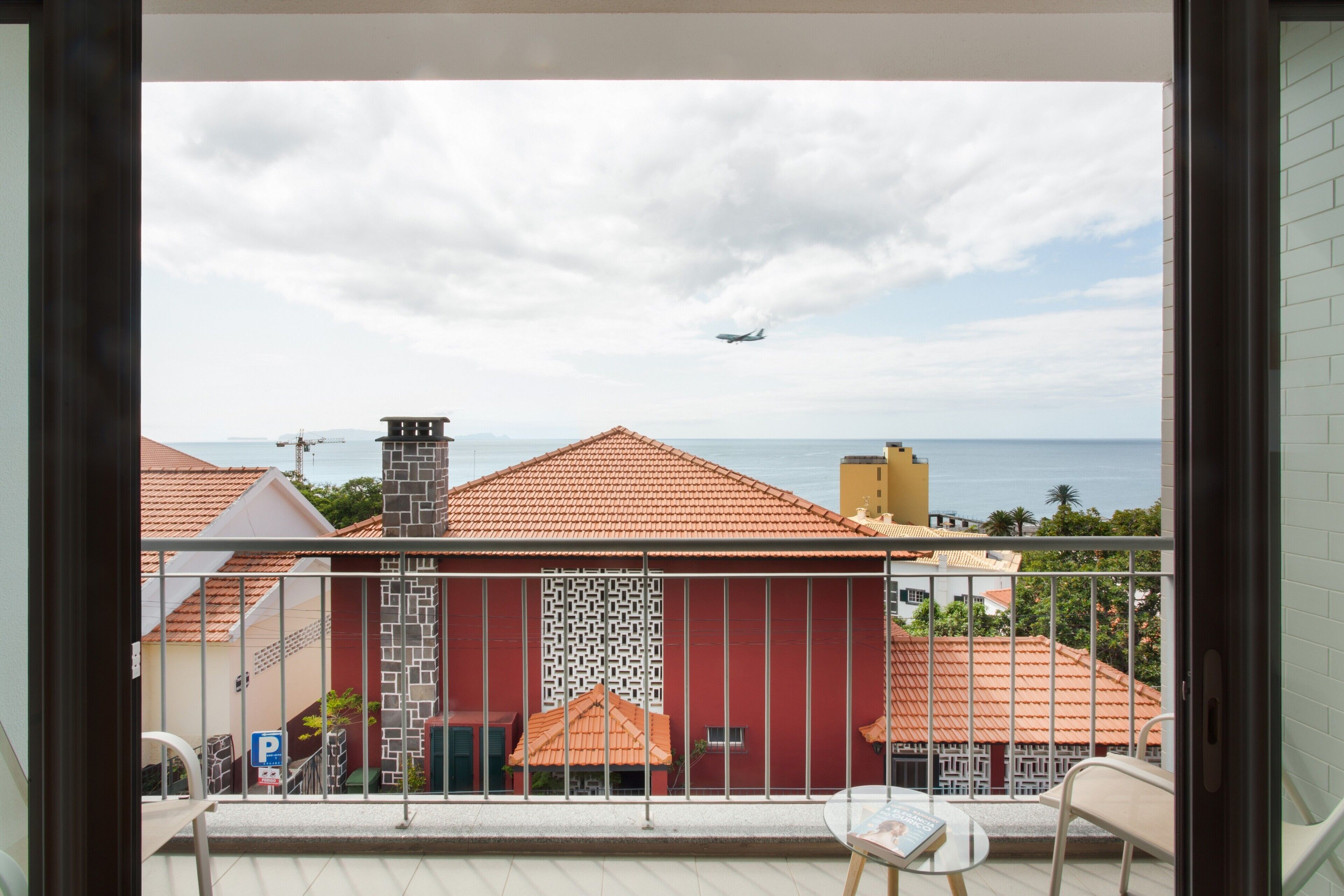 Un balcon avec vue sur la mer et un avion qui se profile à l’horizon.