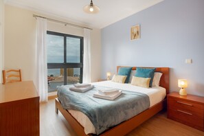 Ein Schlafzimmer mit Bett, Nachttischen, Vorhängen und Meerblick.