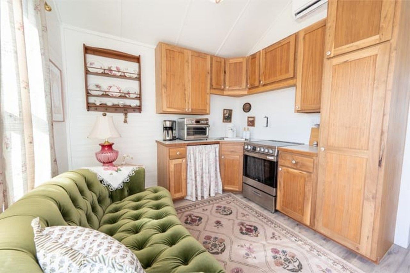 Cozinha compacta com armários de madeira, um sofá verde e um tapete estampado.