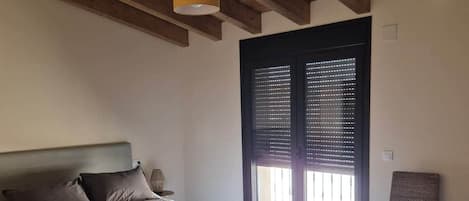 A bedroom with a bed, a chair, a window with blinds, and a wooden ceiling.