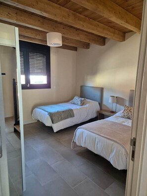 Un dormitorio con dos camas, una ventana con persianas, techo de madera y una mesita de noche con lámpara.