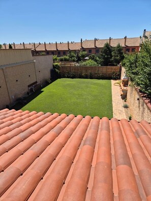 A rooftop terrace with terracotta tiles, a green lawn, and a brick wall.
