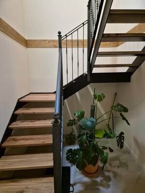 Una escalera de madera con barandilla de metal y una planta en maceta al pie.