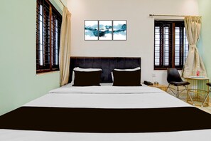 Ein Hotelzimmer mit einem großen Bett, zwei Nachttischen, einem Sessel und einem kleinen Tisch mit Flasche und Glas.