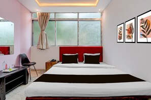 Ein Hotelzimmer mit Bett, Schreibtisch, Stuhl, einem Fenster mit Vorhängen und gerahmten Bildern an der Wand.