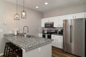 Una cocina moderna con encimera de granito, electrodomésticos de acero inoxidable y una isla central con taburetes de bar.