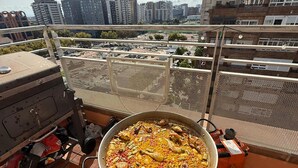Ein großer Topf mit Essen auf einem Balkon, im Hintergrund ist Stadtansicht zu sehen.