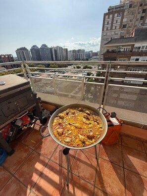 Ein großer Topf mit Essen auf einem Balkon, im Hintergrund ist Stadtansicht zu sehen.