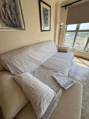 Ein großes, helles Sofa mit gemustertem Bezug und Kissen, platziert in einem Raum mit einem großen Fenster und einem Bild an der Wand.