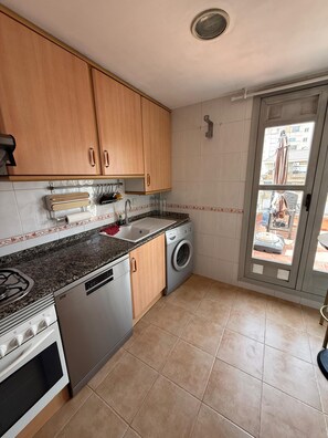 Eine Küche mit Holzausstattung, einem Gasherd, einer Waschmaschine und einem Fenster mit Blick ins Freie.