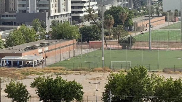 Eine moderne Stadtlandschaft mit Hochhäusern, einem Sportplatz und einem überdachten Bereich mit Tischen und Stühlen.