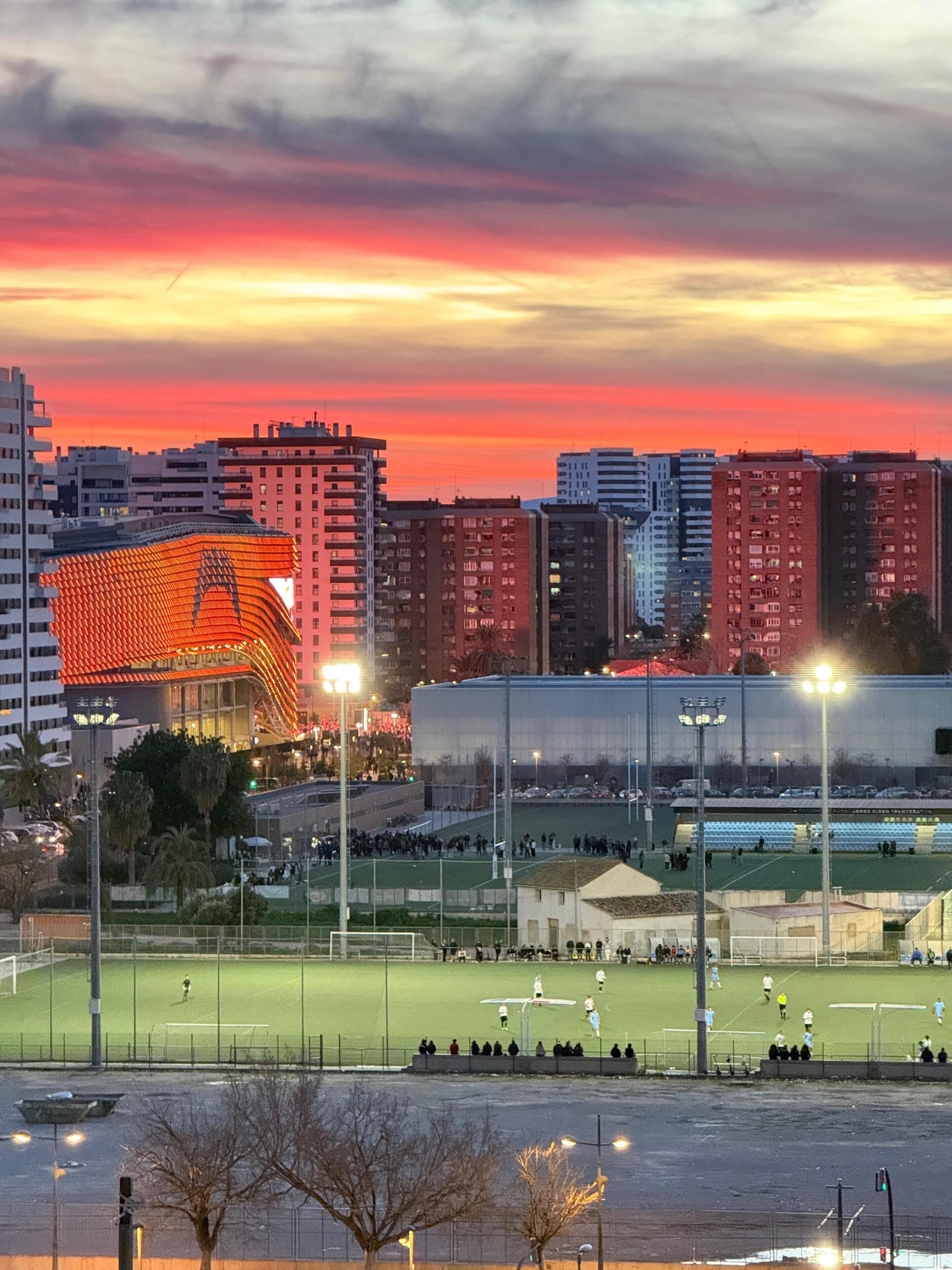 Un stade doté d’un terrain de football, entouré de bâtiments urbains, avec un ciel au coucher du soleil en toile de fond.