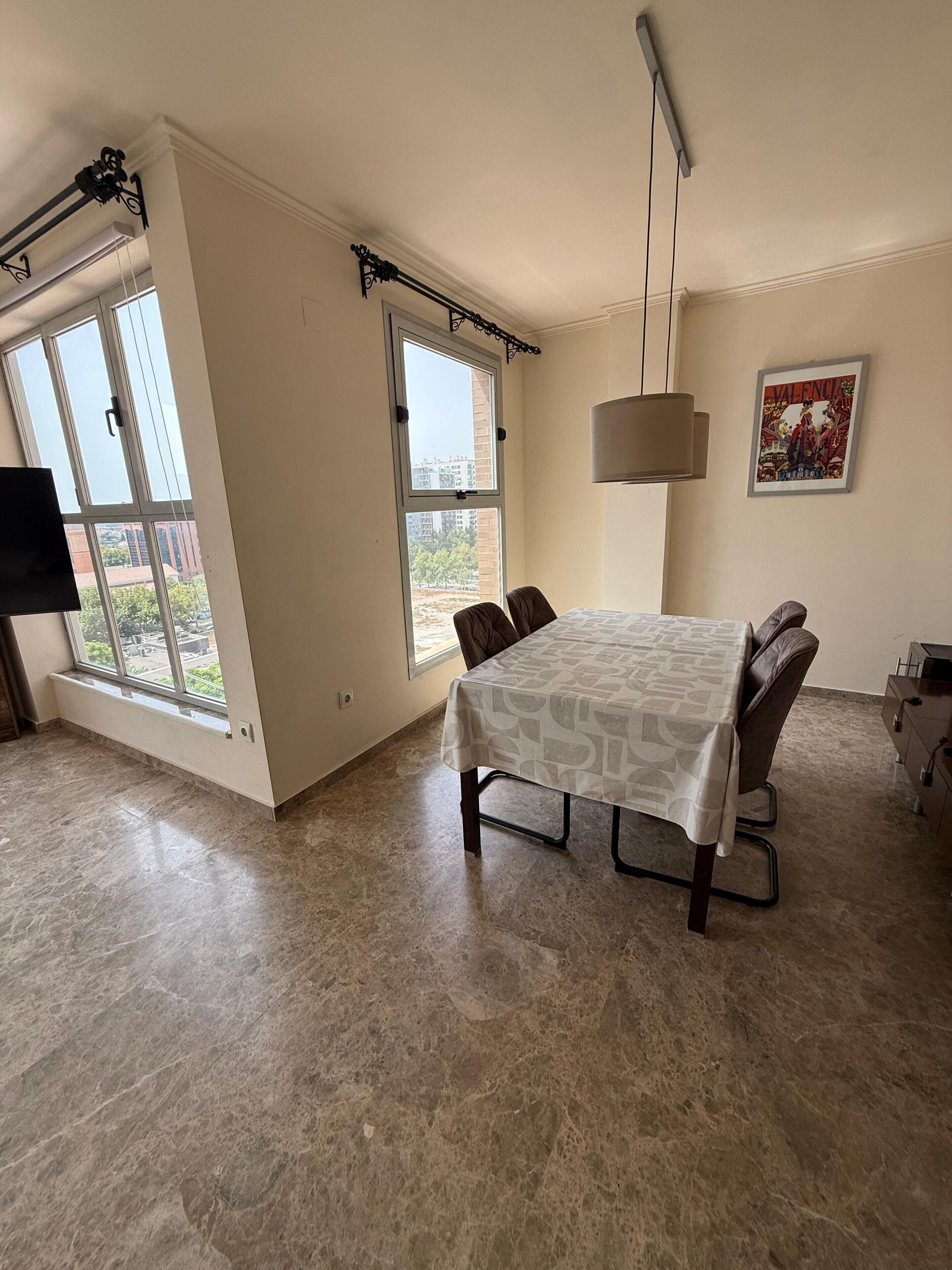 Un espace repas comprenant une table, des chaises, un téléviseur et une fenêtre donnant sur des immeubles.