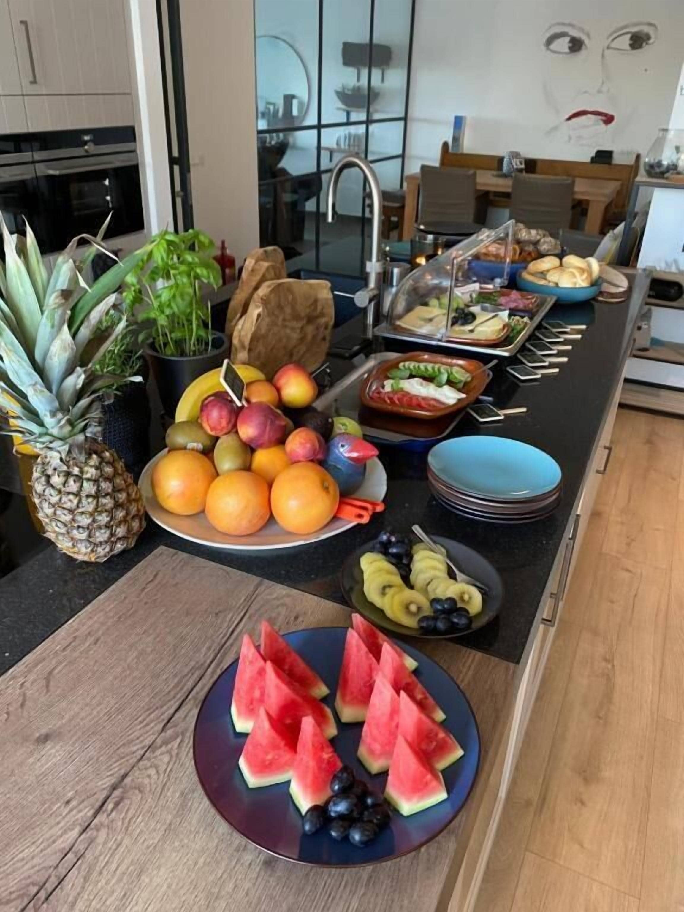 A kitchen counter with various fruits and vegetables, including apples, oranges, and watermelon.