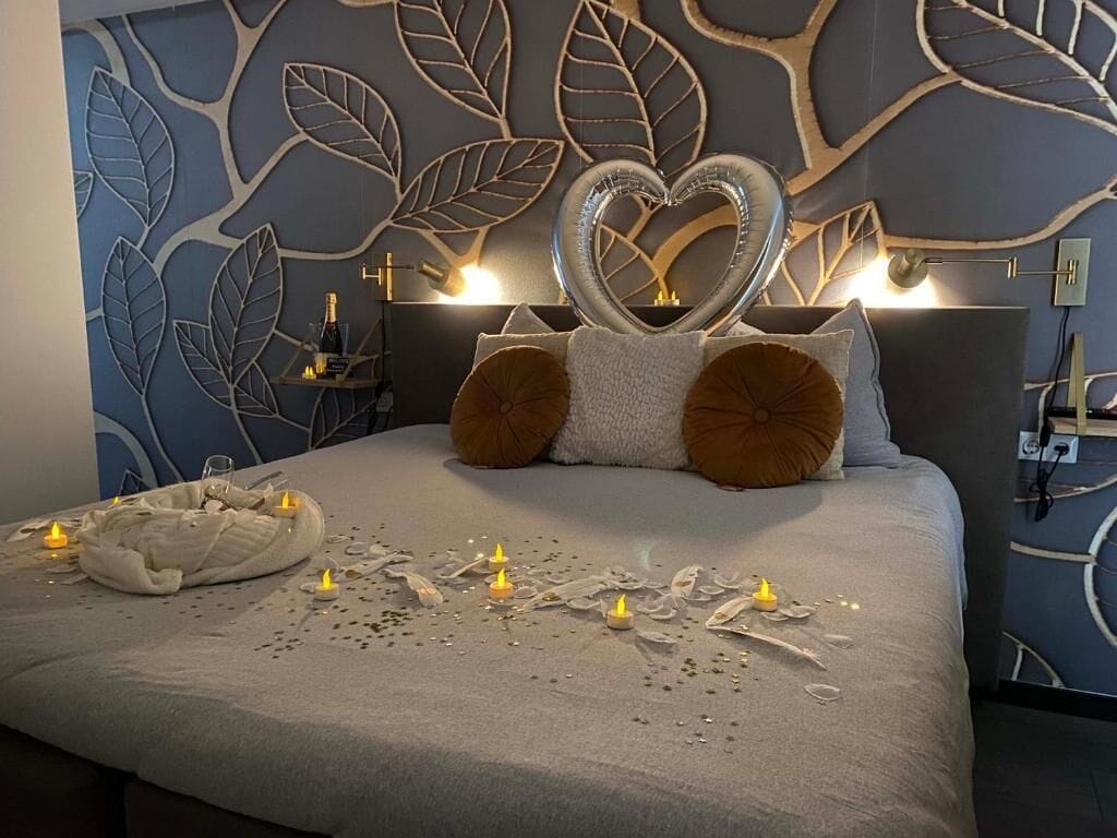 A bedroom with a bed, decorative pillows, a heart-shaped ornament, and candles.
