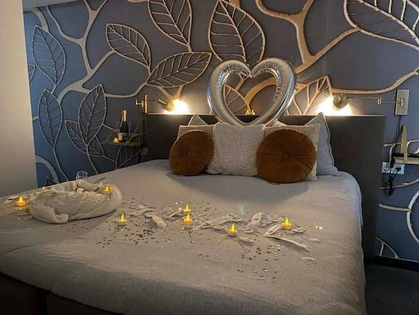 A bedroom with a bed, decorative pillows, a heart-shaped ornament, and candles.