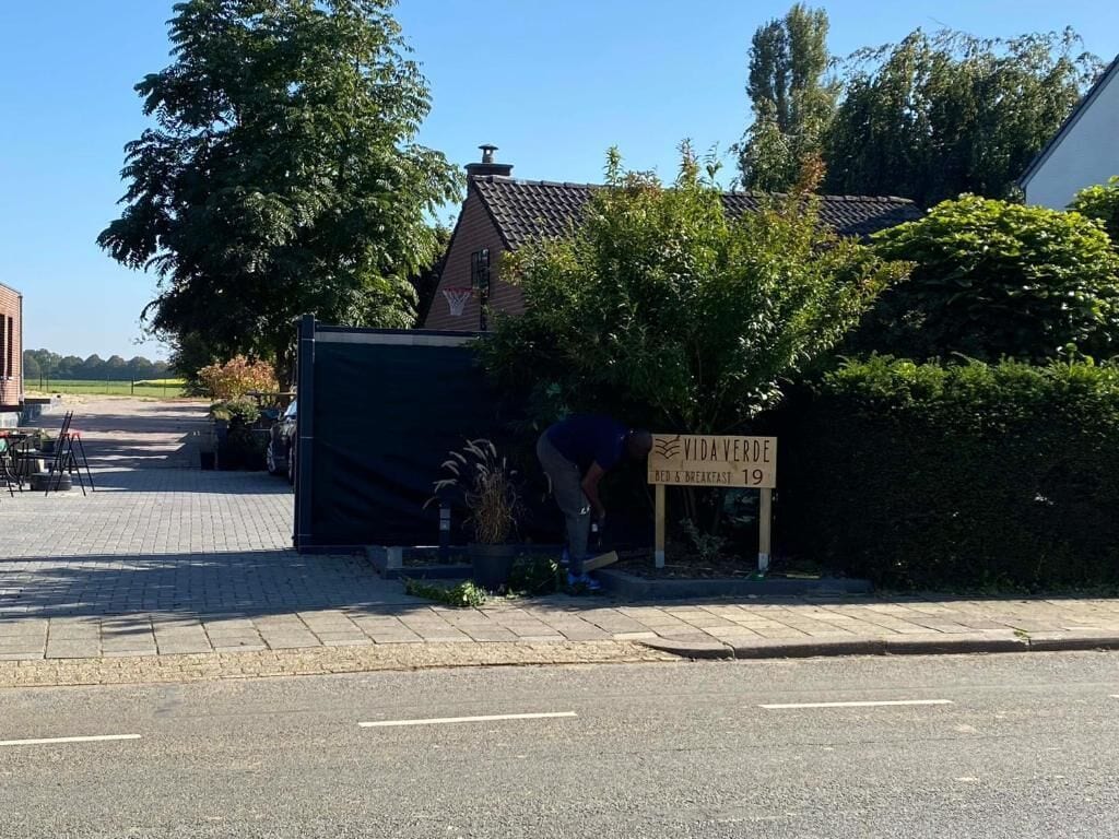 Une enseigne indiquant « VIDAVERDE BED & BREAKFAST 19 », avec une personne s’occupant des plantes.