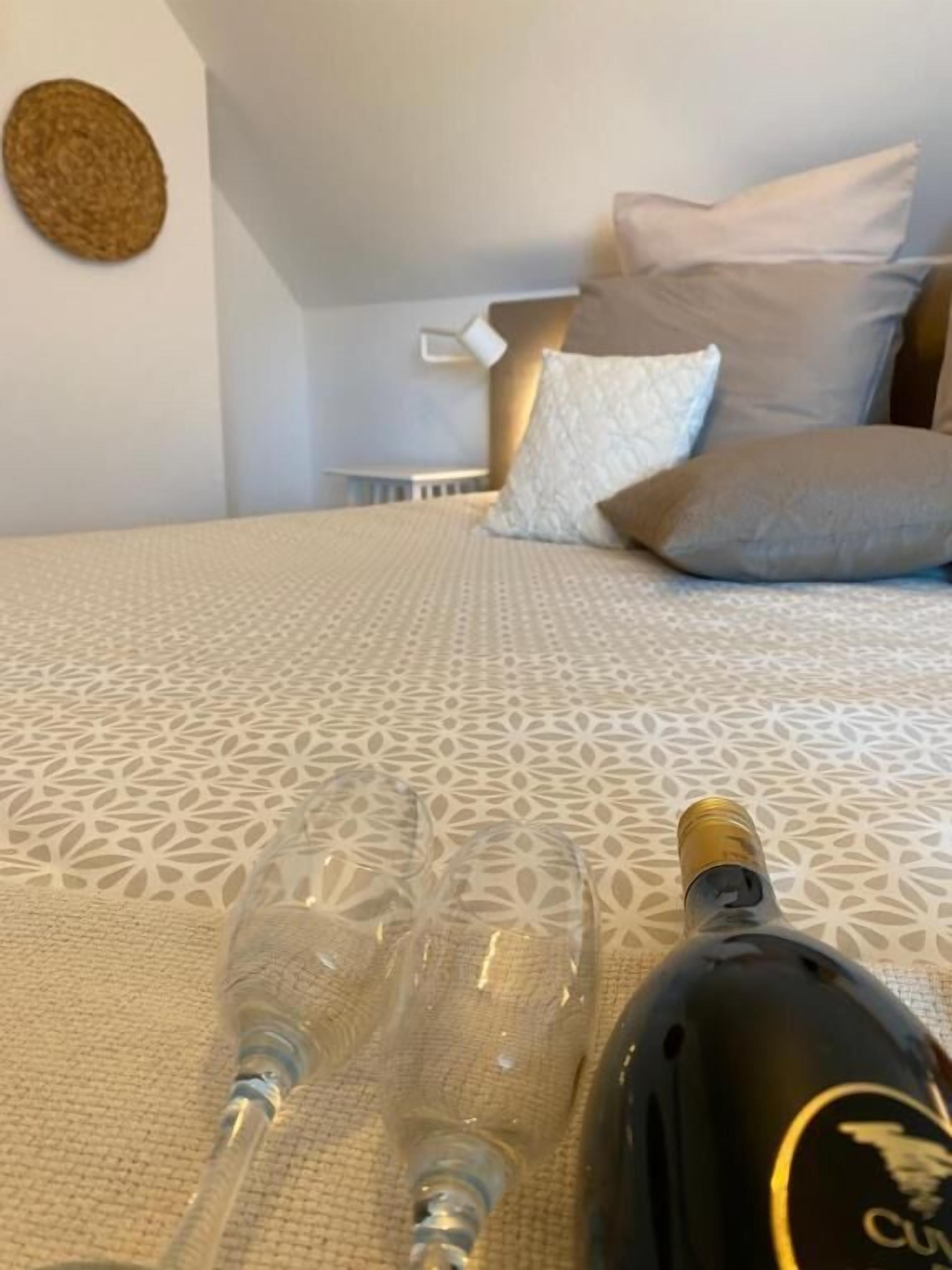 Een bed met een bedsprei met patroon, twee lege wijnglazen en een fles wijn op het bed.