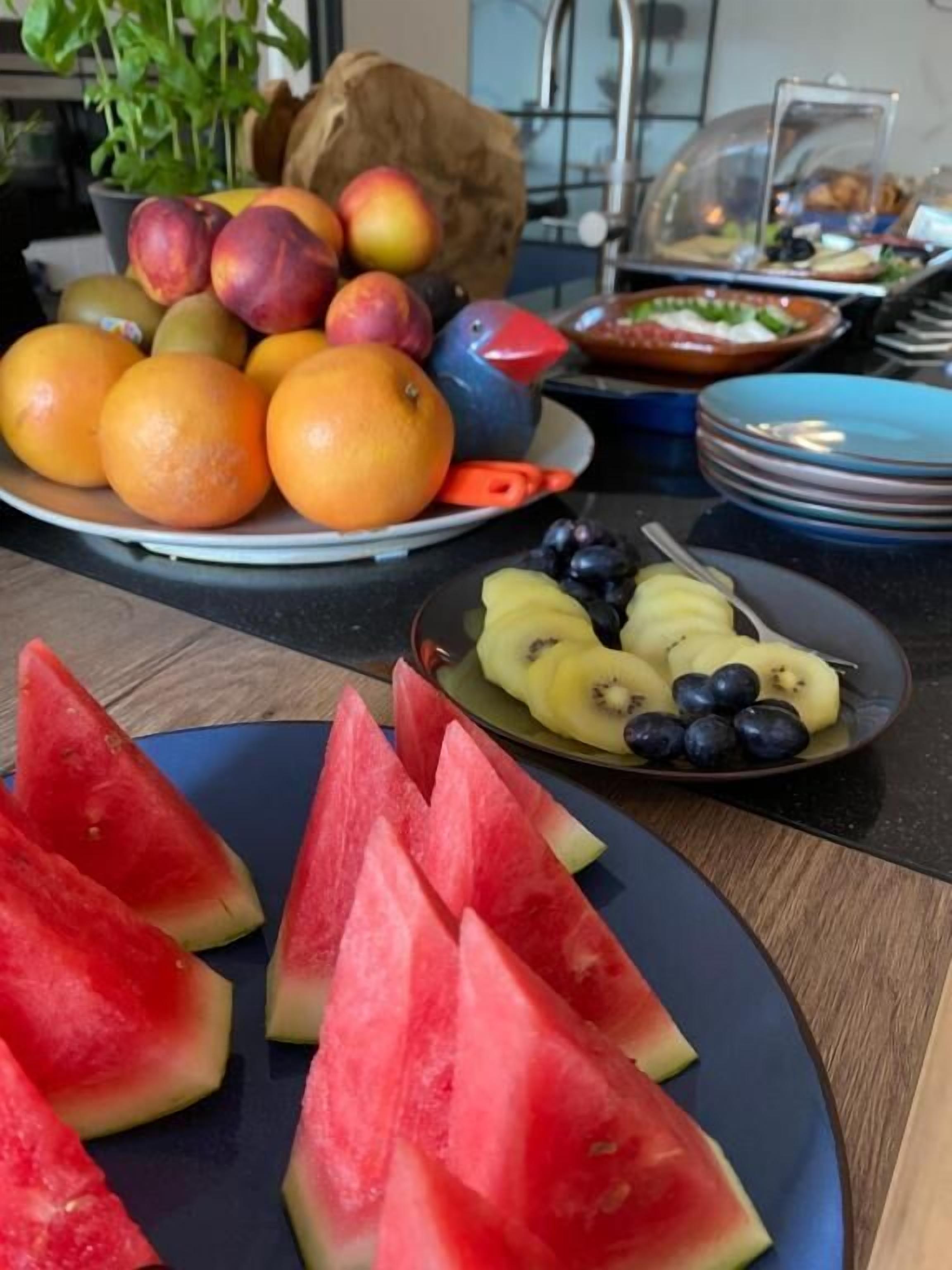 Une variété de fruits est disposée sur une table, notamment des oranges, des pêches et une pastèque.