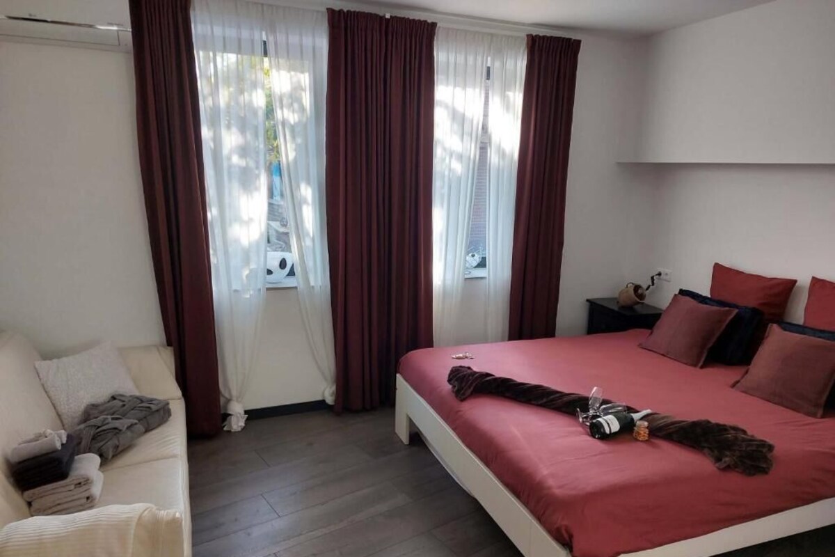 Ein Schlafzimmer mit einem Bett, einem Nachttisch, einer Lampe und einem Fenster mit Vorhängen.