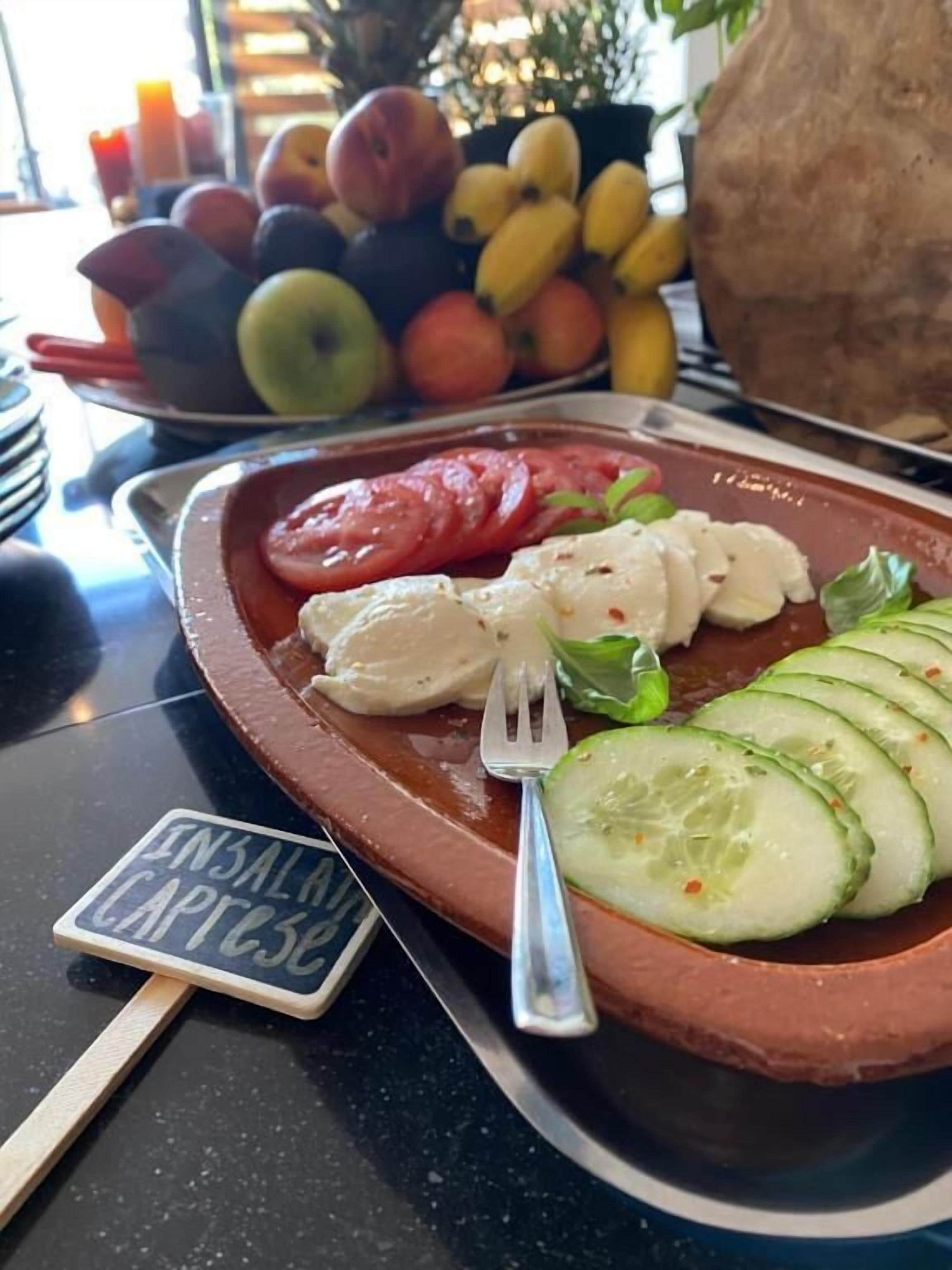 Une assiette de salade caprese, composée de tomates, de mozzarella et de basilic, avec une étiquette noire indiquant « ENSALADA CAPPESE ».