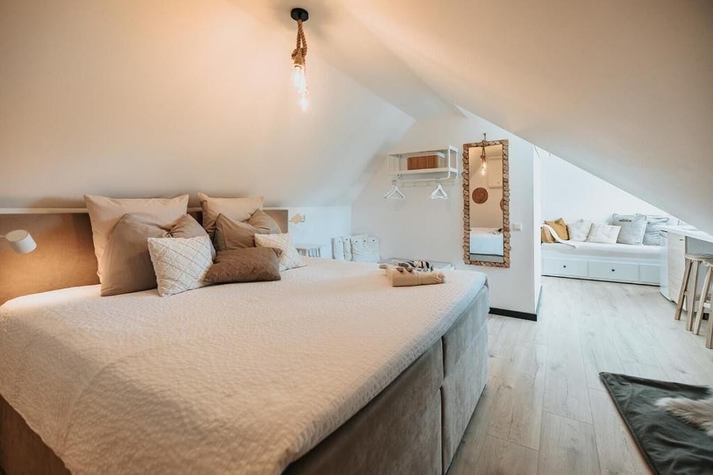 A bedroom with a large bed, a hanging light fixture, and a view of a living area.