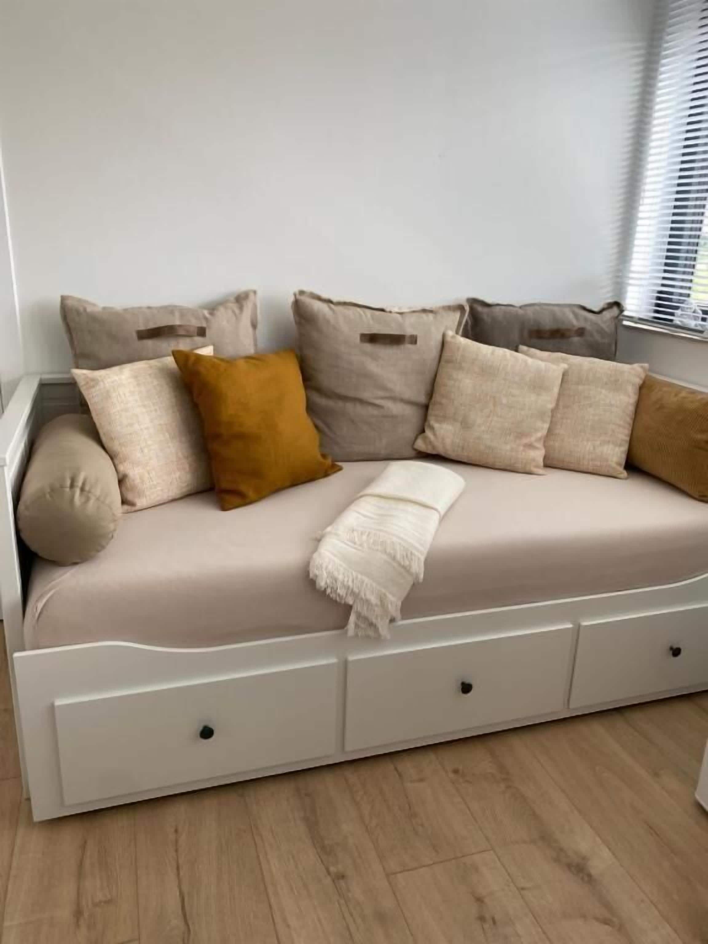 A white sofa with multiple cushions in a neutral color palette, positioned against a light-colored wall.