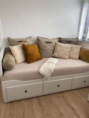 A white sofa with multiple cushions in a neutral color palette, positioned against a light-colored wall.