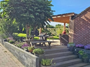 A patio area with a wooden pergola, a brick wall, and a garden with various plants.