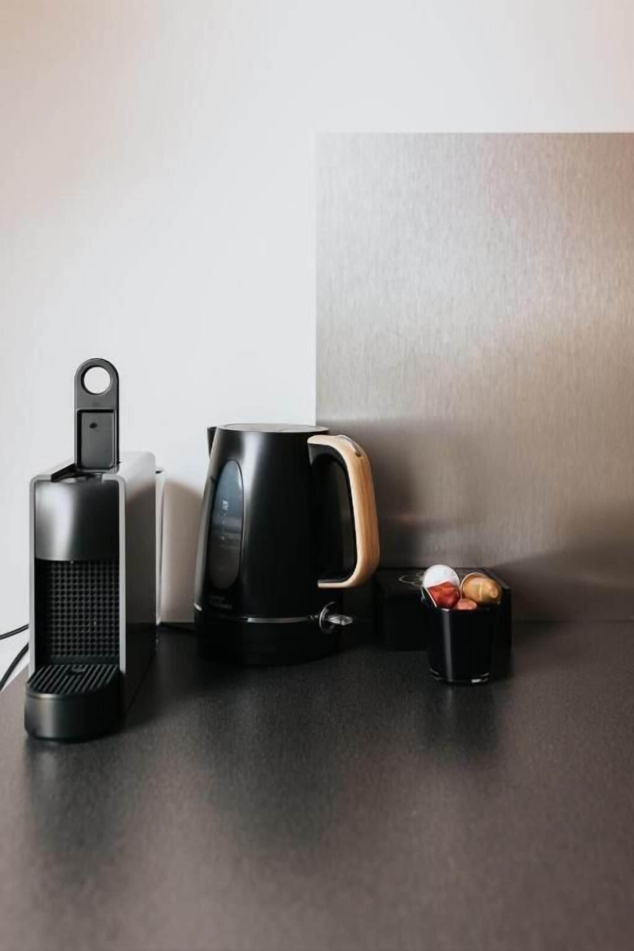 A coffee maker, a mug, and a container with coffee pods on a countertop.