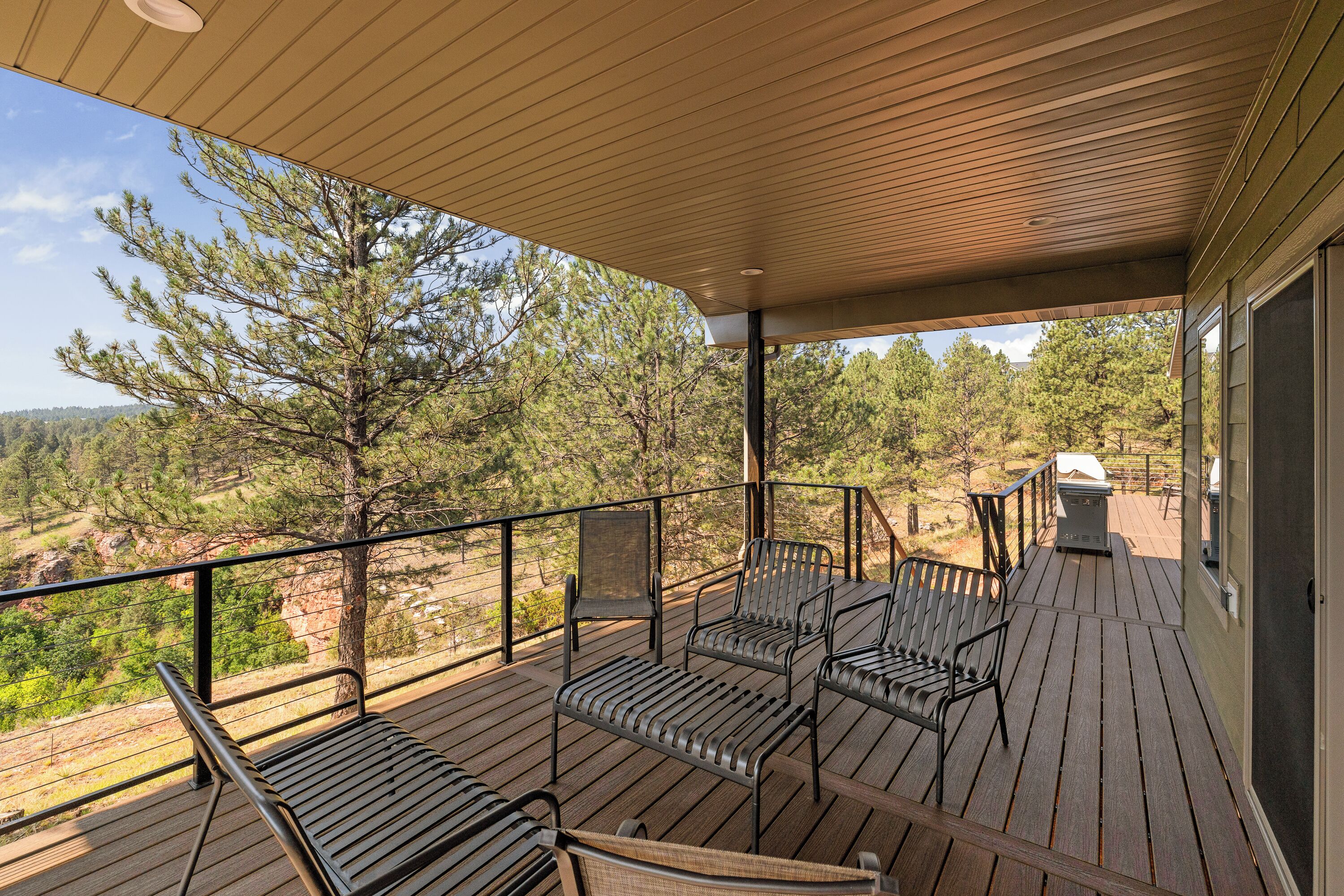 A covered outdoor deck with metal chairs and a grill.