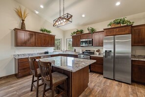 A modern kitchen with wooden cabinets, stainless steel appliances, and a central island with bar stools. - One of a kind view in the south-central Black Hills - Emerald Canyon (Hermosa)