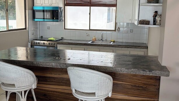 A kitchen with a central island, white bar stools, a microwave, and a stove.