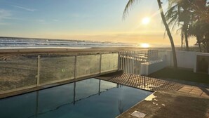 A swimming pool with a view of the beach and ocean at sunset.