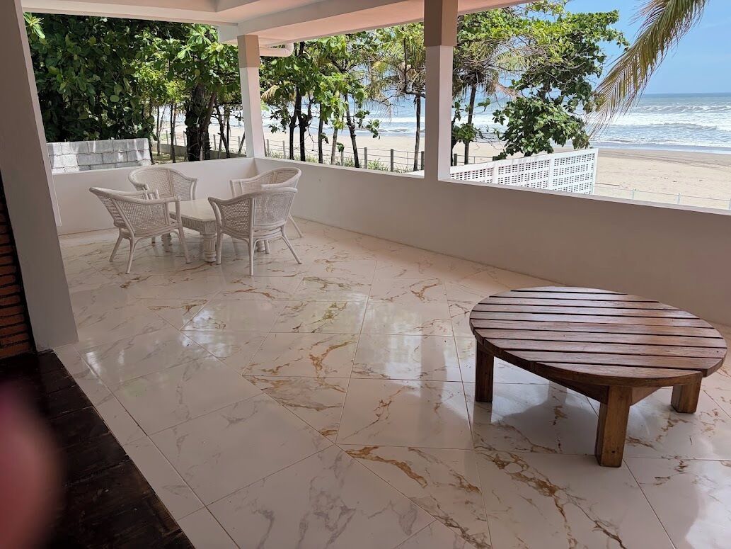 Una habitación con vista al mar, una mesa de madera y sillas de mimbre blanco.