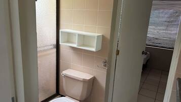 Un baño pequeño con inodoro, un estante blanco y una ventana con persianas.