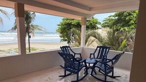 A covered patio with a view of the beach, featuring a table and four chairs.