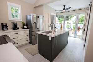 A modern kitchen with a central island, stainless steel appliances, and a sliding glass door leading to a patio. - Lighthouse Suites Collection (Key West)