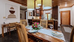 A dining area with a wooden table set for four, surrounded by chairs, with a kitchen in the background. - Three bedroom  in Costa Rica, Playa Langosta (Tamarindo)