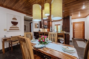 A dining area with a wooden table set for four, surrounded by chairs, with a kitchen in the background. - Three bedroom  in Costa Rica, Playa Langosta (Tamarindo)